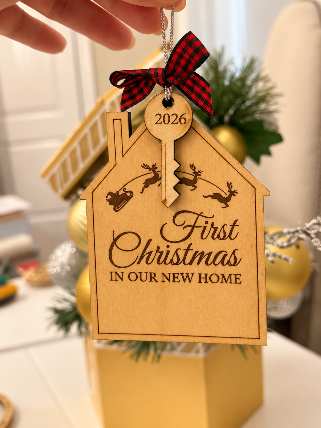 A hand holds a personalized wooden house-shaped Christmas ornament engraved with &