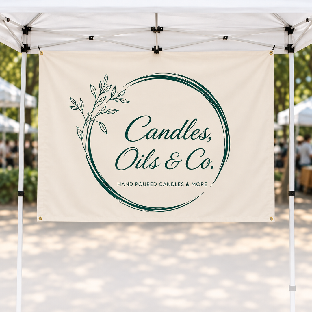 A cream-colored promotional banner hanging from a white pop-up canopy at an outdoor market. The banner features a dark green circular brushstroke design with a leafy branch on the left and the text &