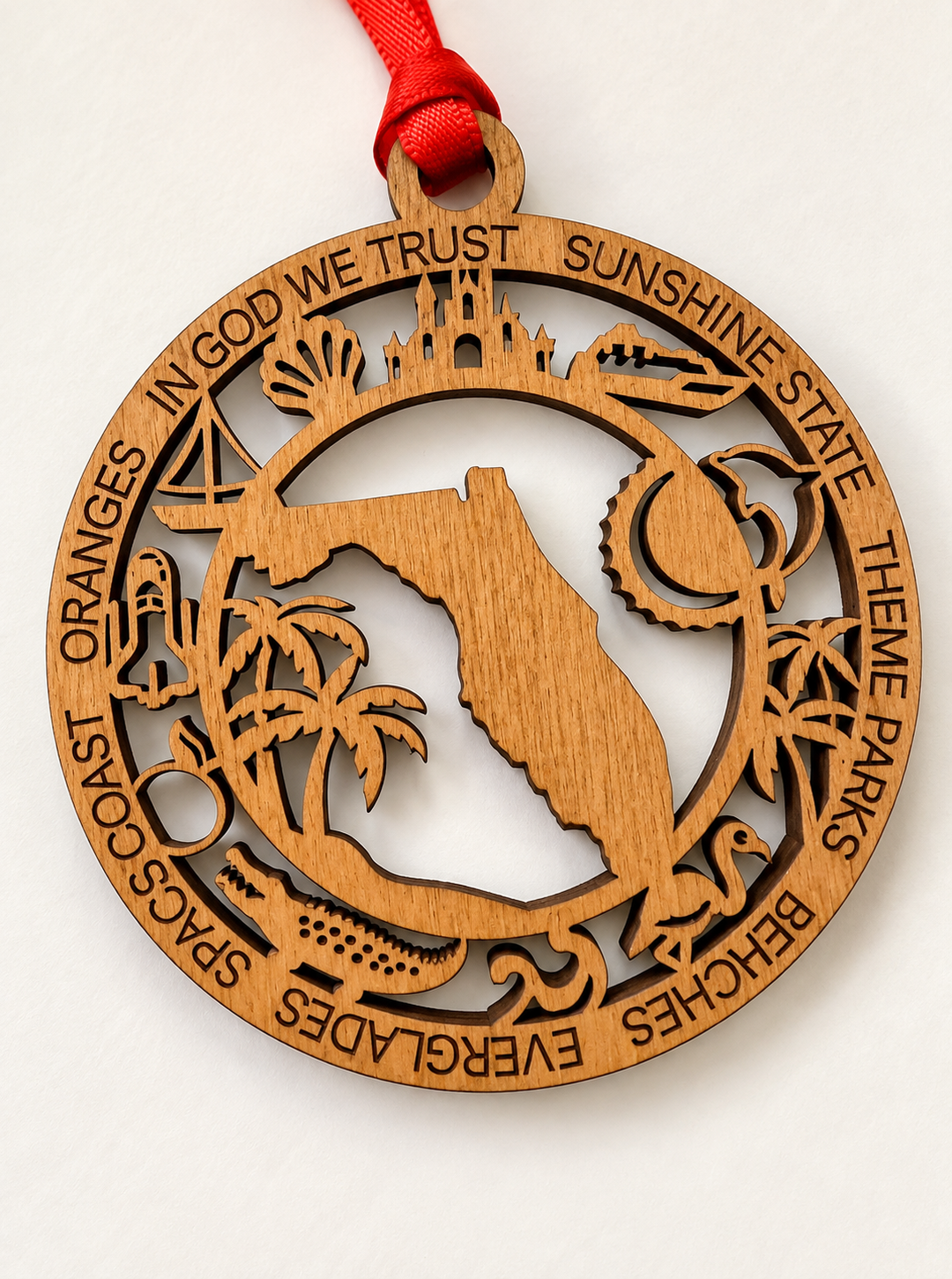 A round laser-cut wooden ornament featuring the Florida state silhouette in the center, surrounded by engraved beach and Florida landmarks and text including &